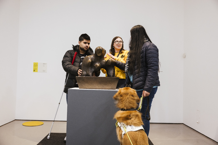 Two visitors and a Guide Dog with an Information Assistant interacting with  Henry Moore Mother and Child: Arch 1959. Photo Joanne Crawford